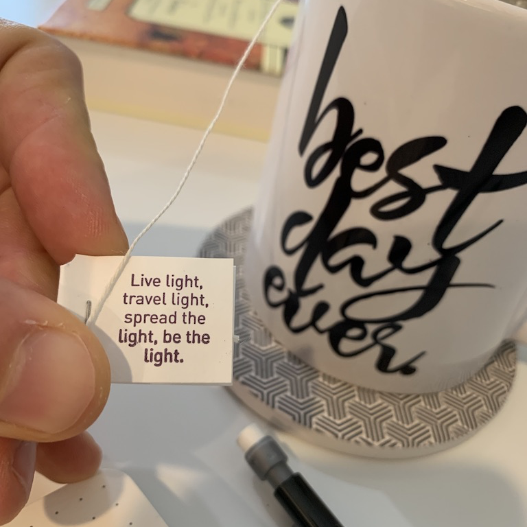 A teacup printed best day ever with a Yogi Tea tag held up reading: live light, travel light, spread the light, be the light.