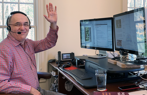 Stephen Wolfram waving at his dual-monitor home office: the left monitor shows email and chat, the right monitor screenshares to meeting attendees.
